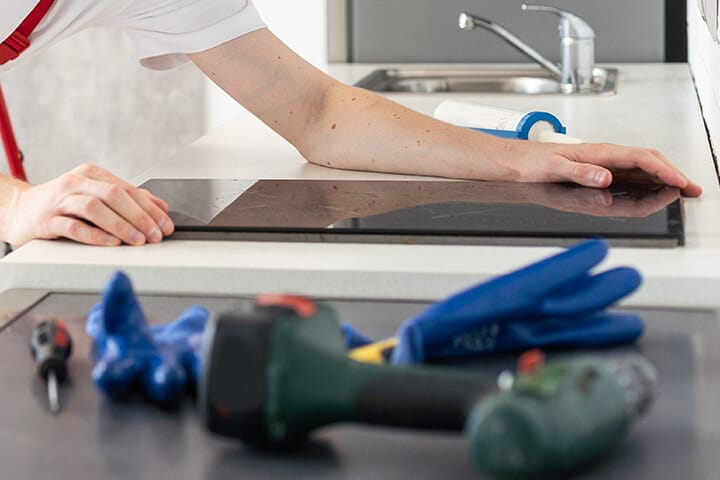 gloved craftsman installs hob in kitchen