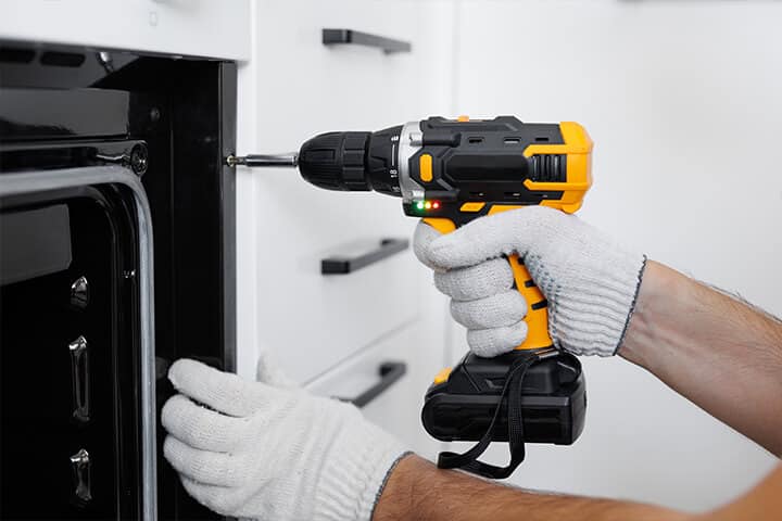 man installs the oven after assembling the kitchen and screws the bolts with a screwdriver